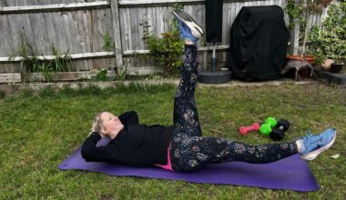 Kat Storr doing Pilates scissors exercise on yoga mat in garden