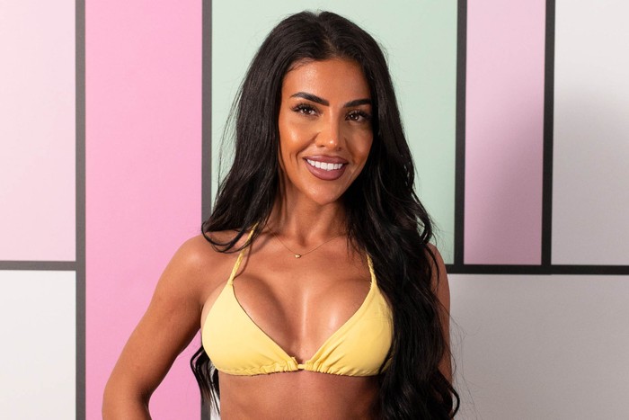 love-island (50) A woman with long black hair, smiling ahead with one hand on her hip. She is wearing a yellow bikini.