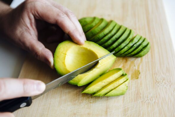 Man slicing avocado with a knife on a cutting board close up Man slicing avocado with a knife on a cutting board close up
