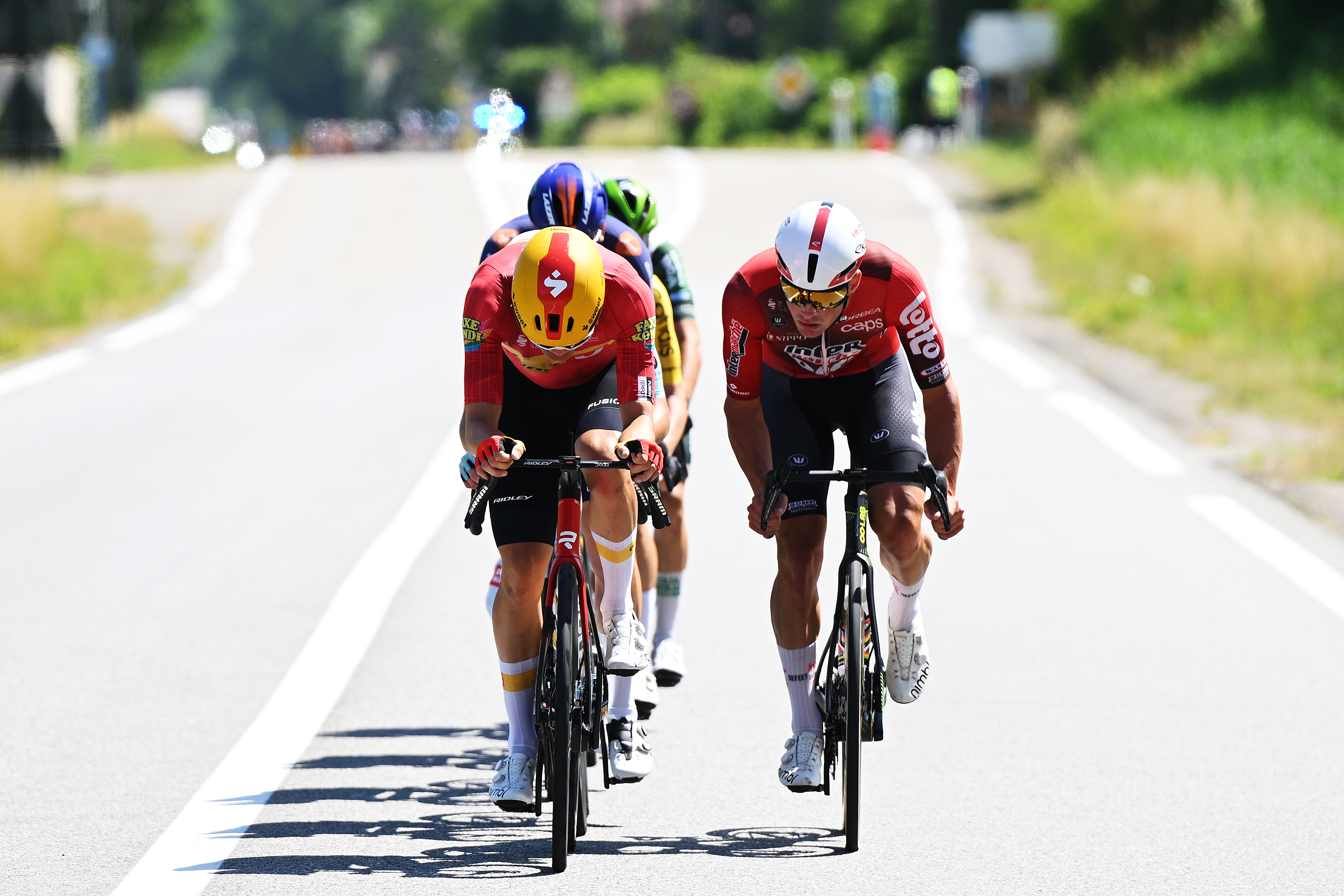 Six riders on a two-lane road in bright sunlight