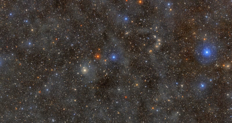 A colorful expanse of deep space filled with countless stars and cosmic dust, featuring bright blue, red, and orange stars scattered across the dark, speckled background.