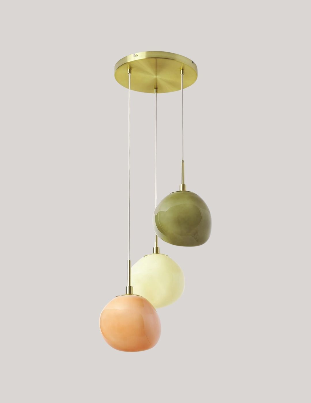 A three-part pendant light made of organically shaped, semi-spherical pendants in nude, beige, and dark green, set against a pale brown background.
