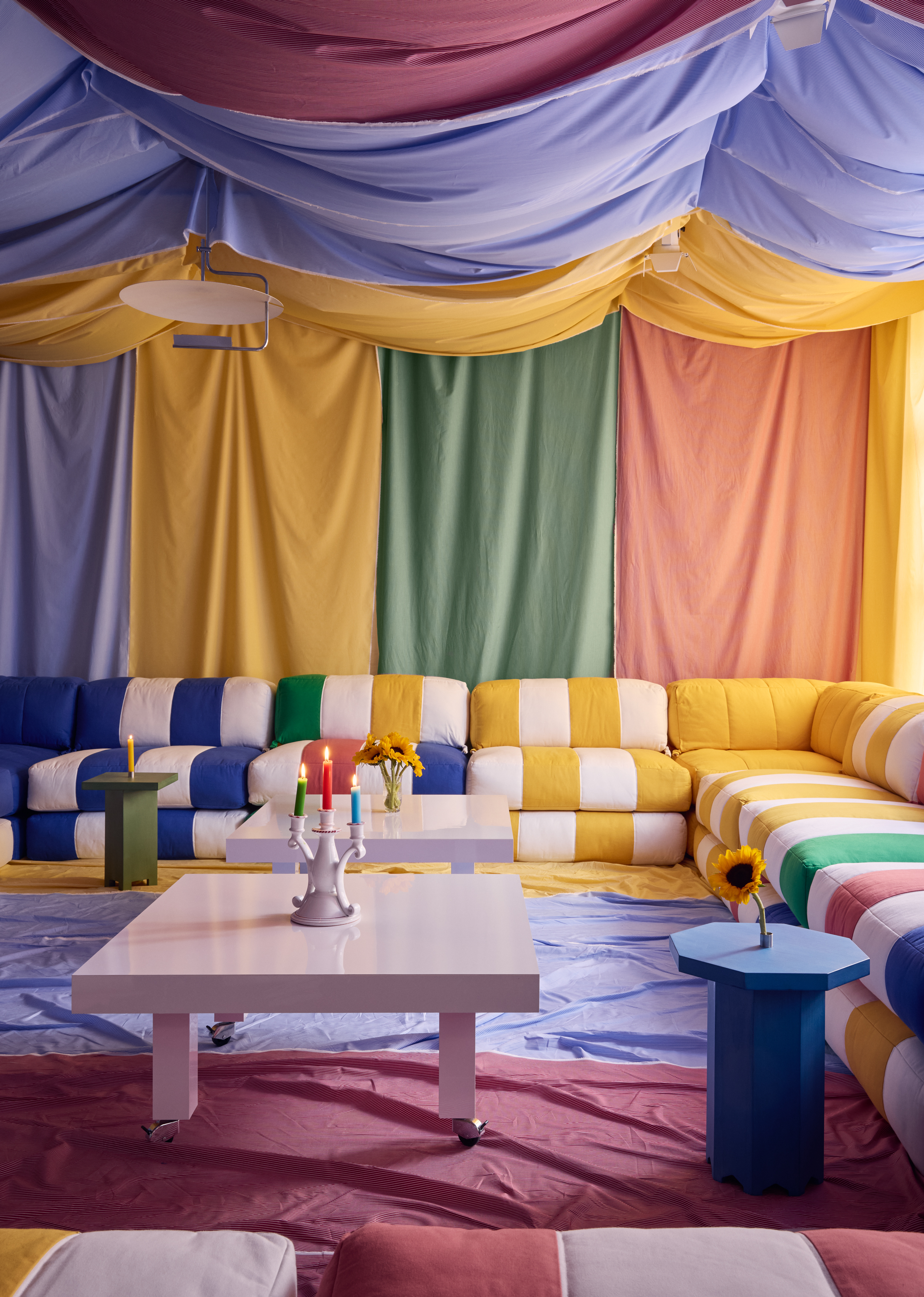 a room draped in colorful fabric with multicolor striped sofas and fabric on the floor