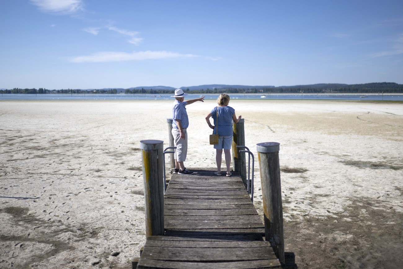 Two people on a jetty are looking out over a dried-up lake