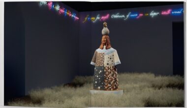 an open book spread with a grassy installation surrounding a figurative sculpture with neon text around the room