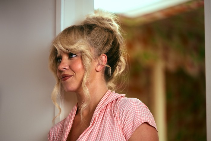 euphoria-sydney-sweeney_10 Sydney Sweeney as Cassie Howard in a pink blouse stands in a doorway with her hair up in the Euphoria season 3 finale.