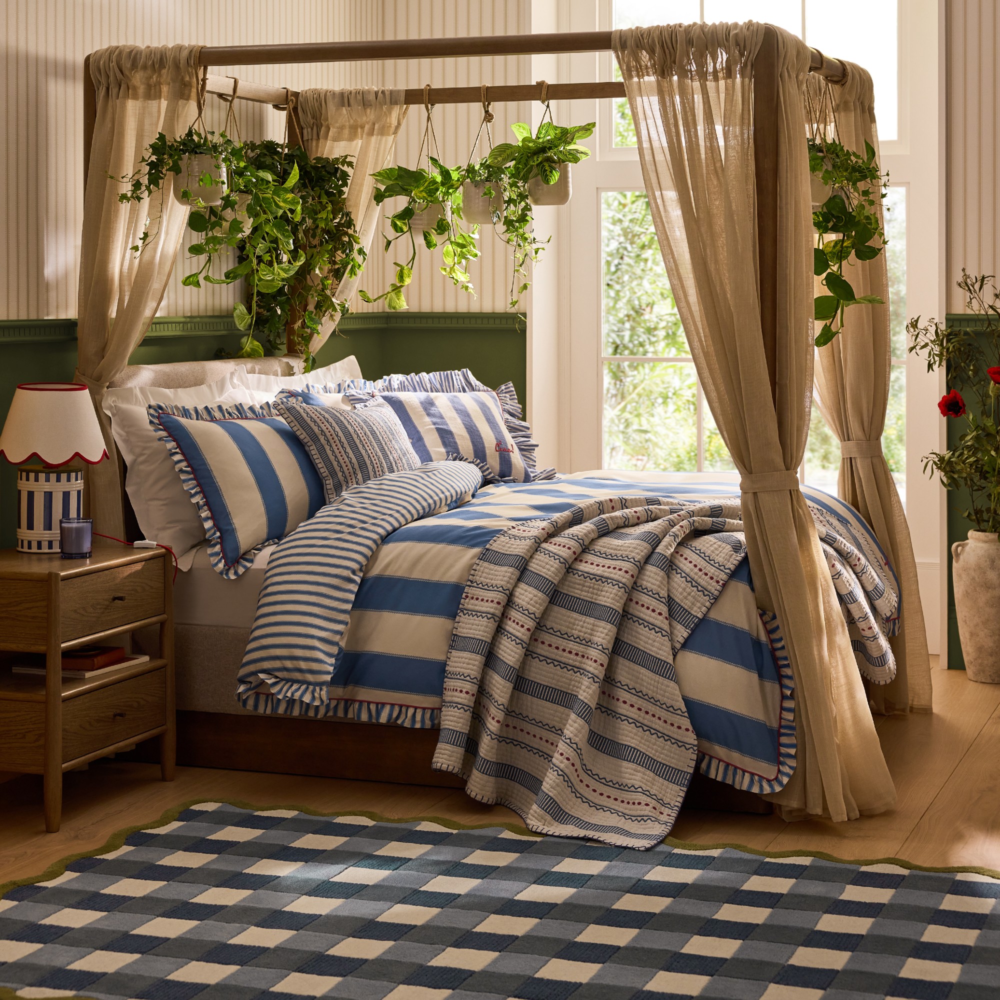 A bedroom with a canopy bed decorated with pieces from the Next x Lia Gold collection including blue and white striped bed linen and a gingham rug