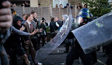 A group of white men faces off against police with riot shields in a suburban English street.