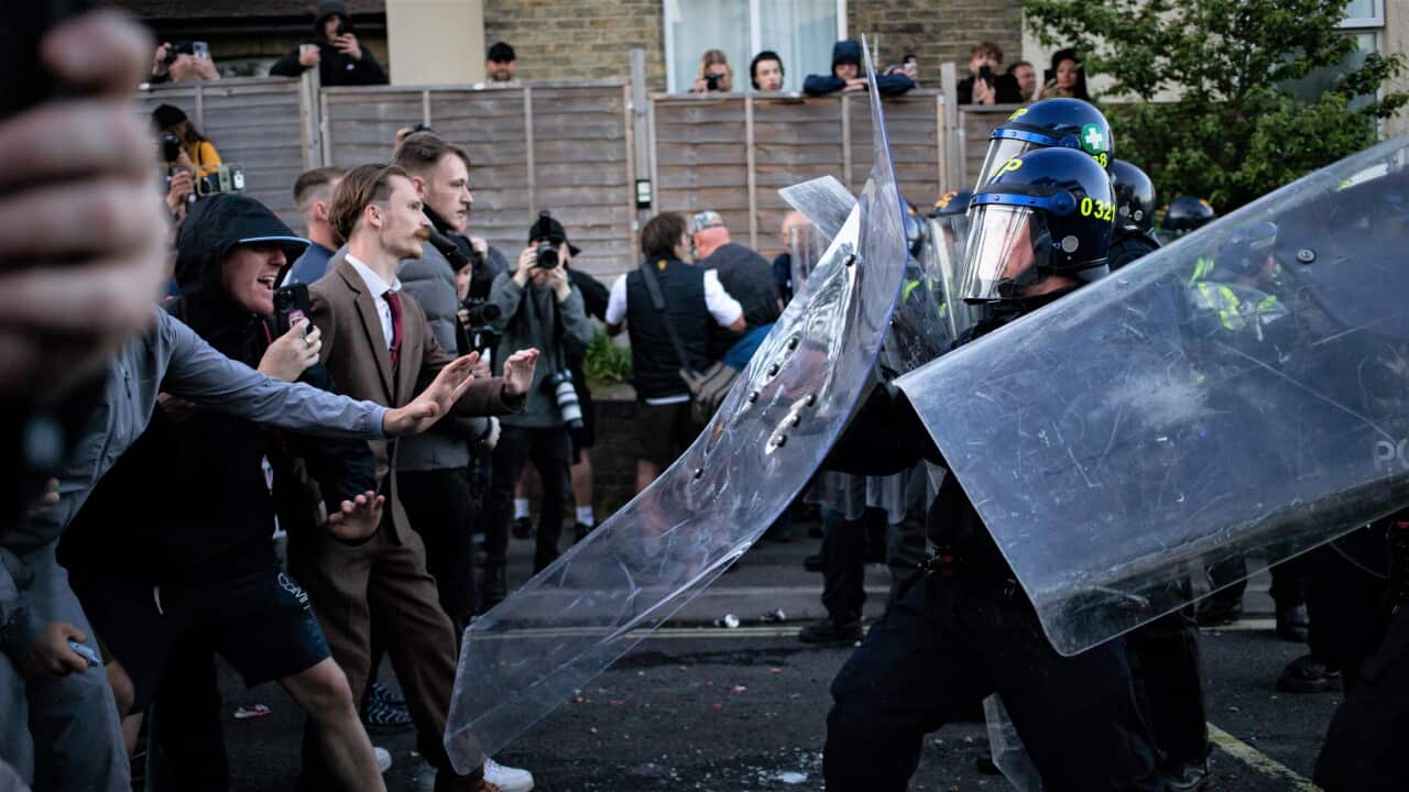 A group of white men faces off against police with riot shields in a suburban English street.