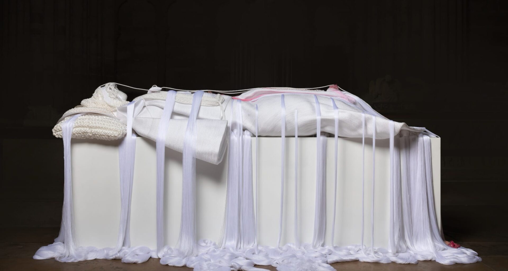 a mixed media white rope sculpture of a female figure laying down, referencing noble sculptures on top of sarcophagi, with draping ropes pooling at the floor