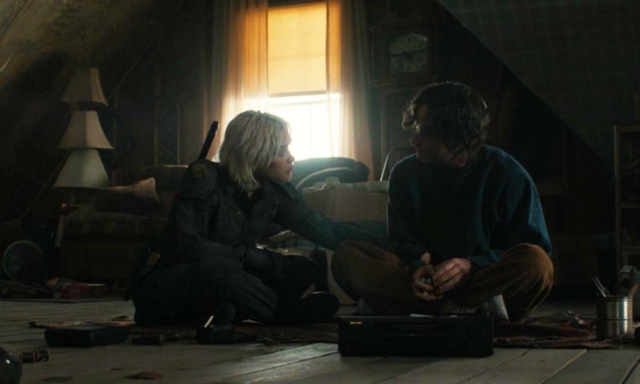 Two people sitting on the floor in a dimly lit room, holding hands and talking.