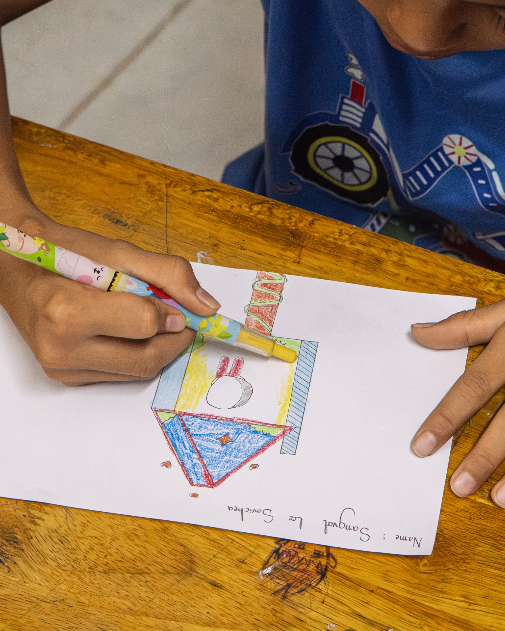 a child draws a birdhouse design with colored pencils