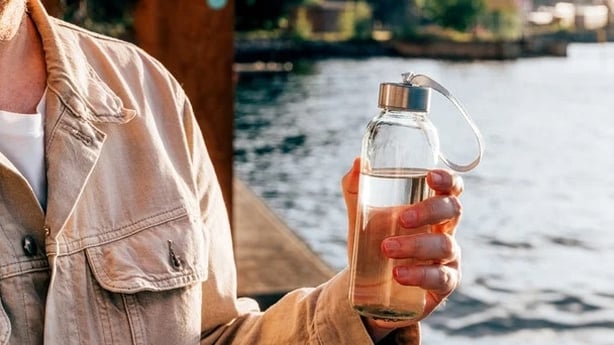 A person holds a bottle of water near a river