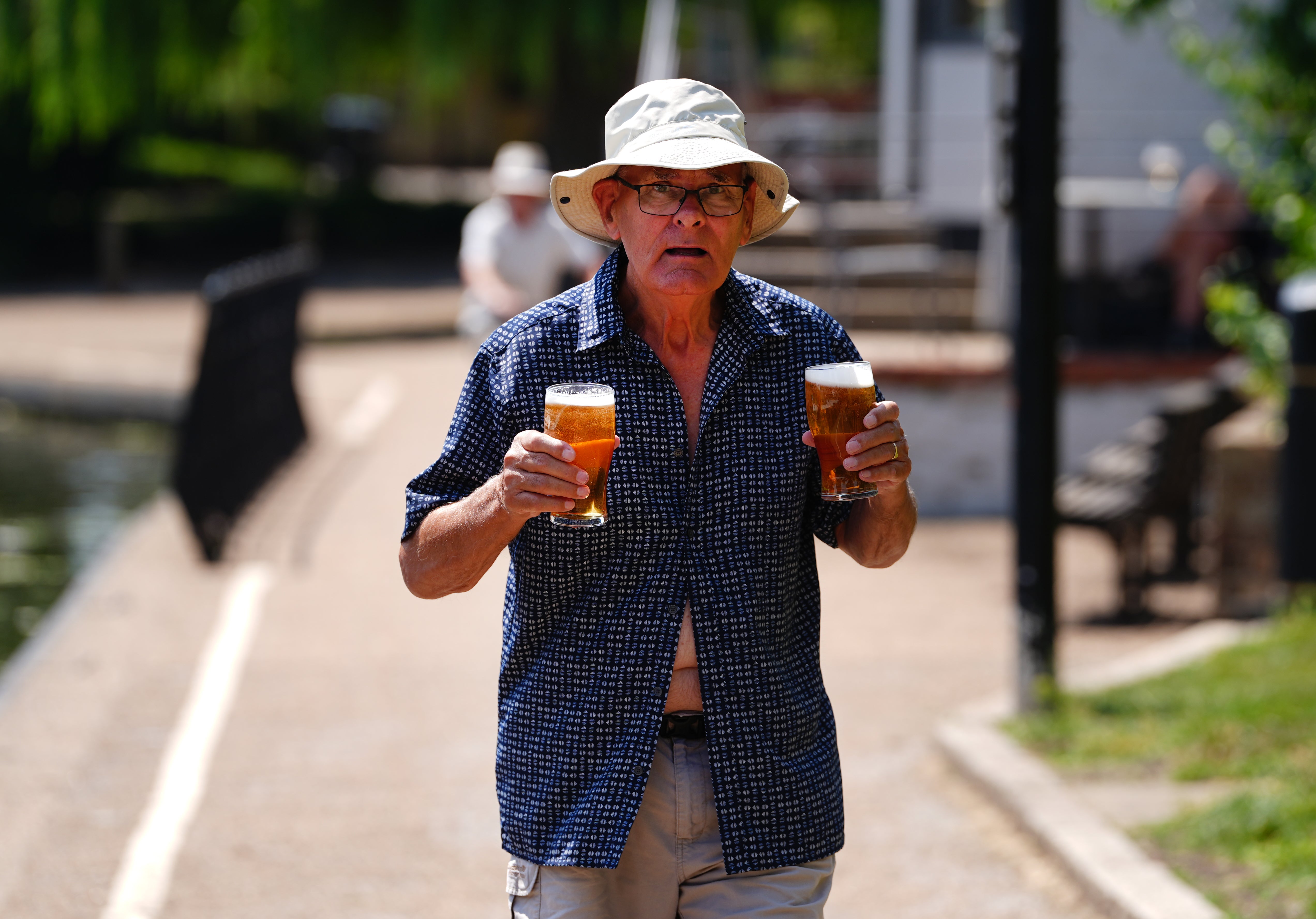 A man holds two pints as he walks next to the River Great Ouse in Ely during the last heatwave
