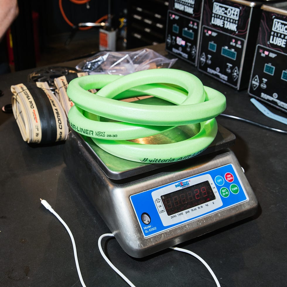 A digital scale displaying a green bicycle tire liner alongside various tools and equipment in a workshop setting.