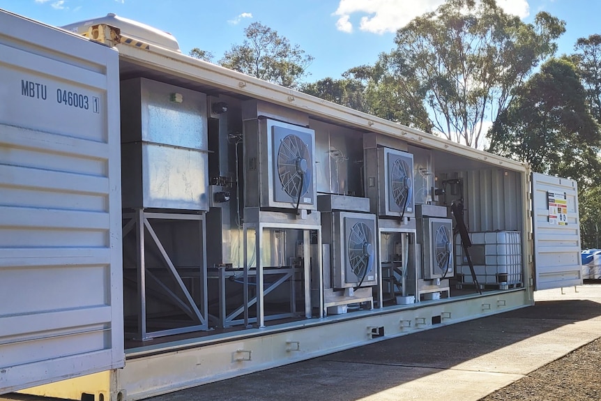 An open sea container with a machine inside showing boxes and fans.