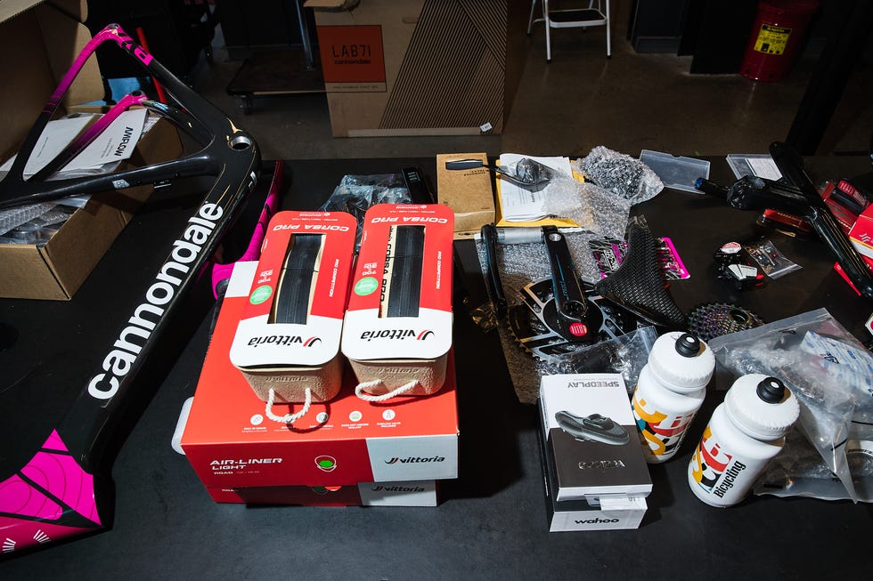 Various cycling components, including a bike frame, tires, tools, and accessories on a work surface.