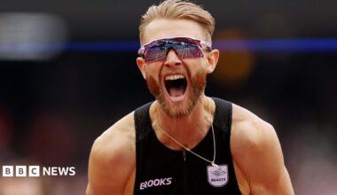 Josh Kerr roars with delighted after breaking the mile record. he has blonde hair and a beared and is wearing a black running vester and reflective wraparound sunglasses.