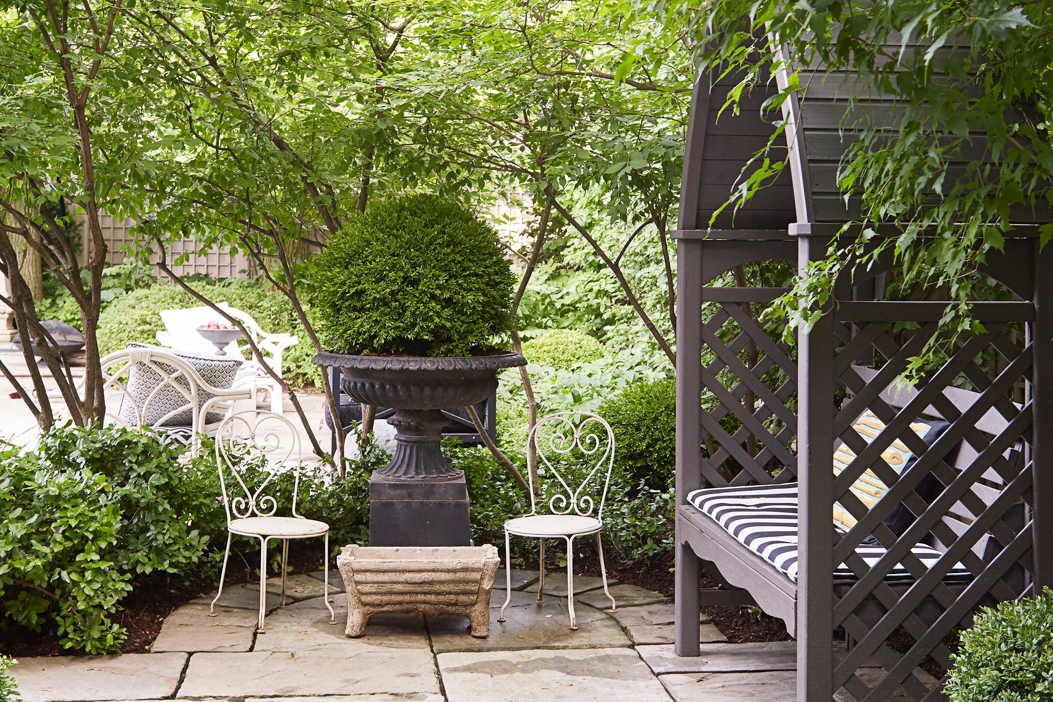 VER040118_091 A peaceful garden setting with lush greenery, decorative chairs, and a stone pathway.