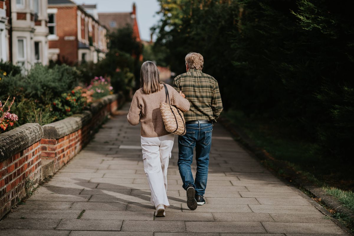 A mature couple walk arm-in-arm down a footpath in a residential district