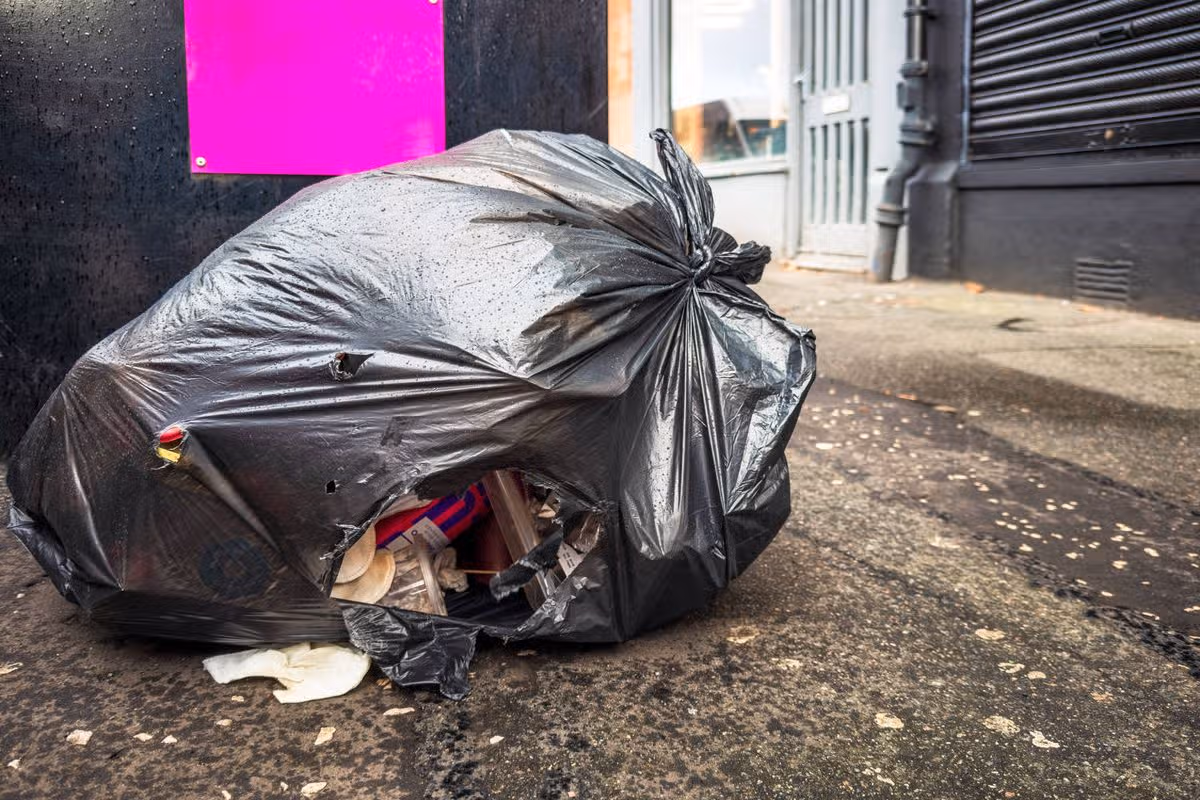 A large hole from in a plastic bin bag, left next to a full litter bin on a pavement in Glasgow.
