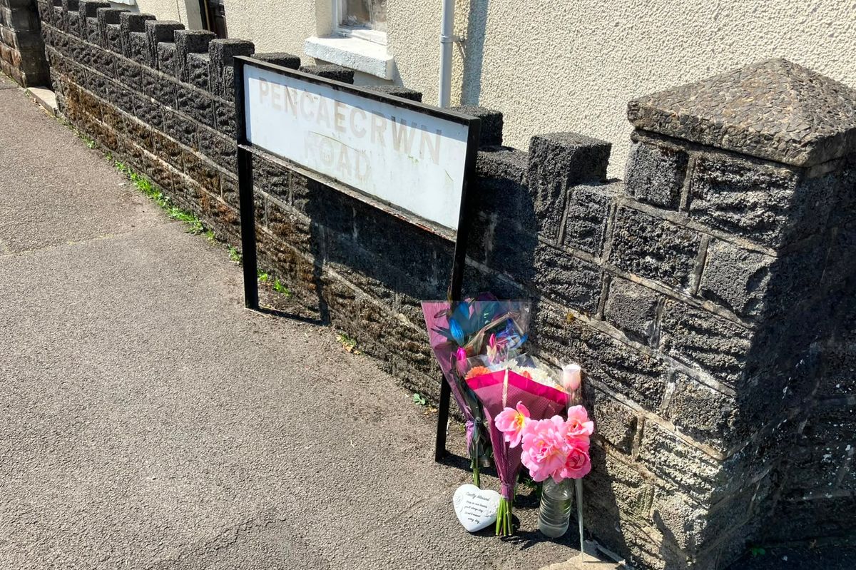 Floral tributes left at a road sign reading Pen Cae Crwn Road