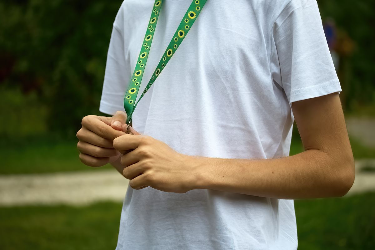 Sunflower lanyard, symbol of people with invisible or hidden disabilities. A person wearing a white shirt fiddles with a green lanyard adorned with sunflower designs.