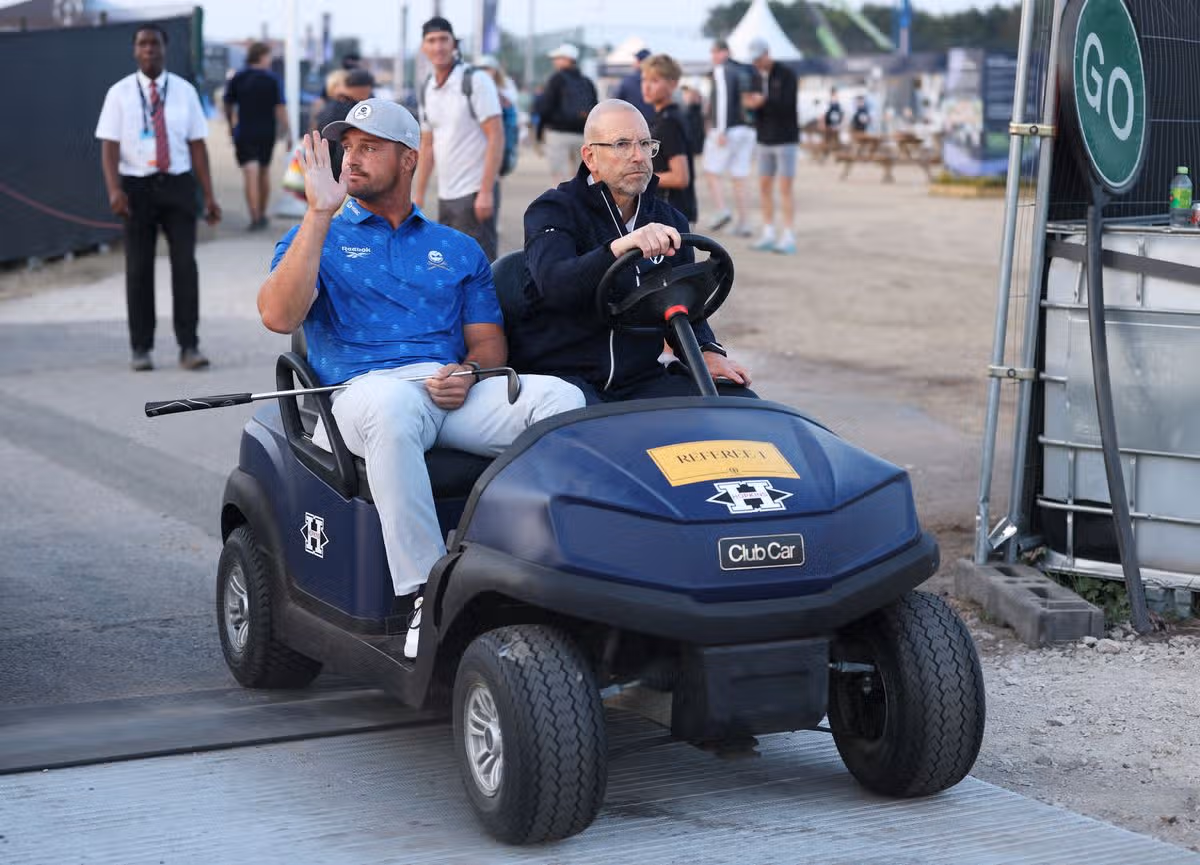 Bryson DeChambeau is driven by a rules offical on a buggy to the recorders area