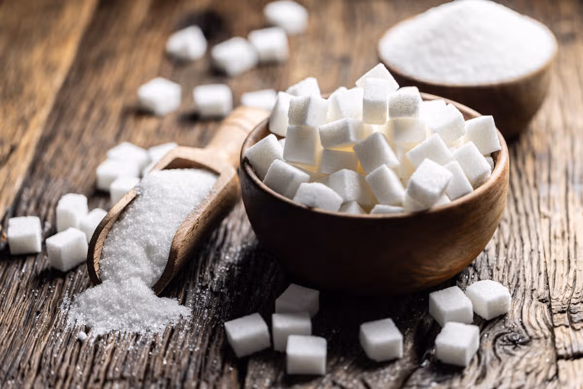 Granulated sugar in a wooden scoop or bowl on an old oak table.