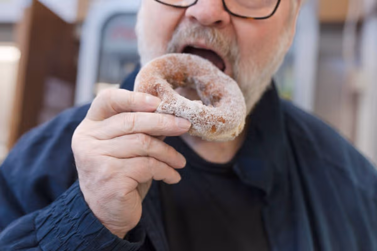 Senior man enjoying a sugar-coated doughnut at a bakery or cafe. High quality photography, 2026.