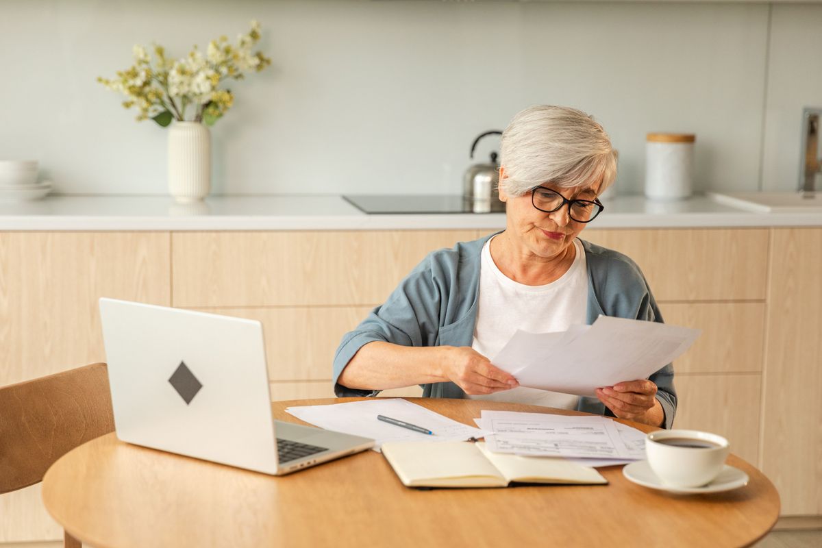 An elderly woman sitting at a table looking at paperwork.