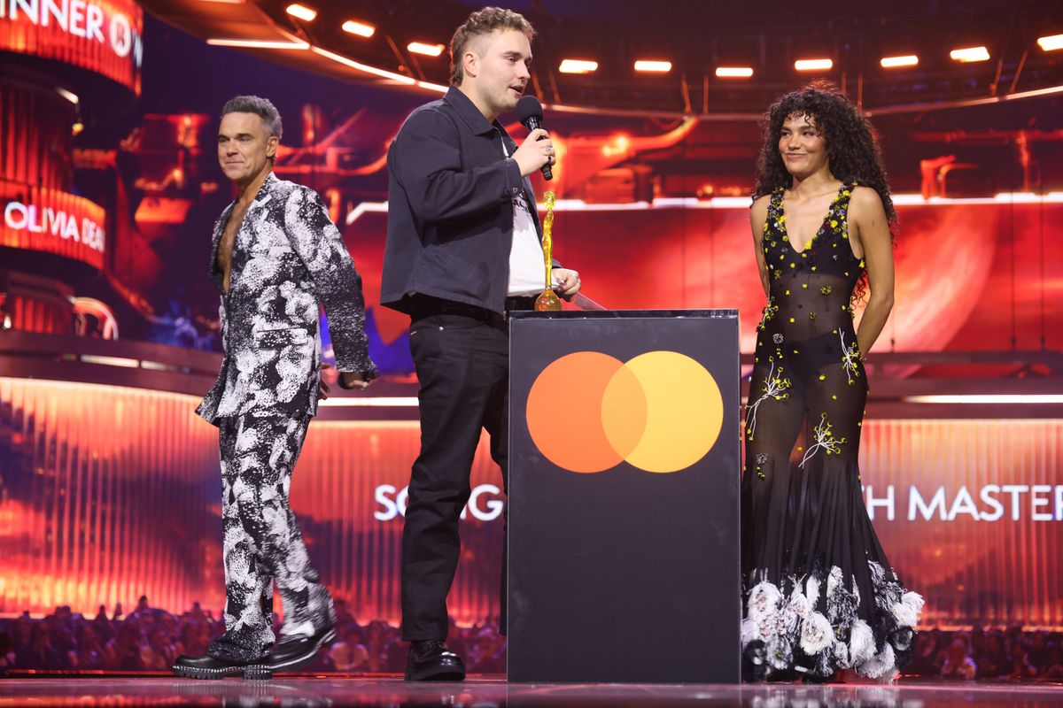 Sam Fender on stage accepting the 'Song of the Year' award with Olivia Dean and Robbie Williams