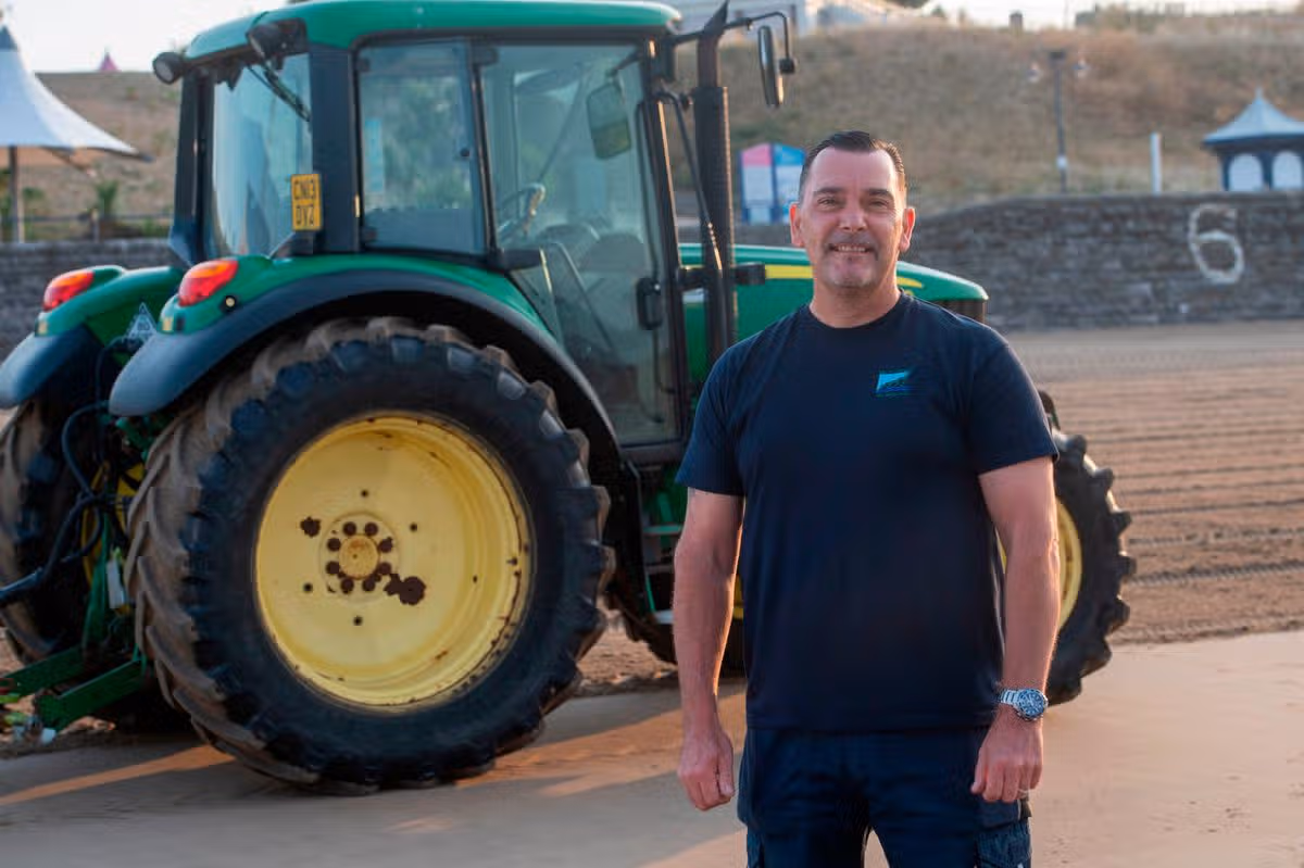 A man stood next to a tractor on a beach