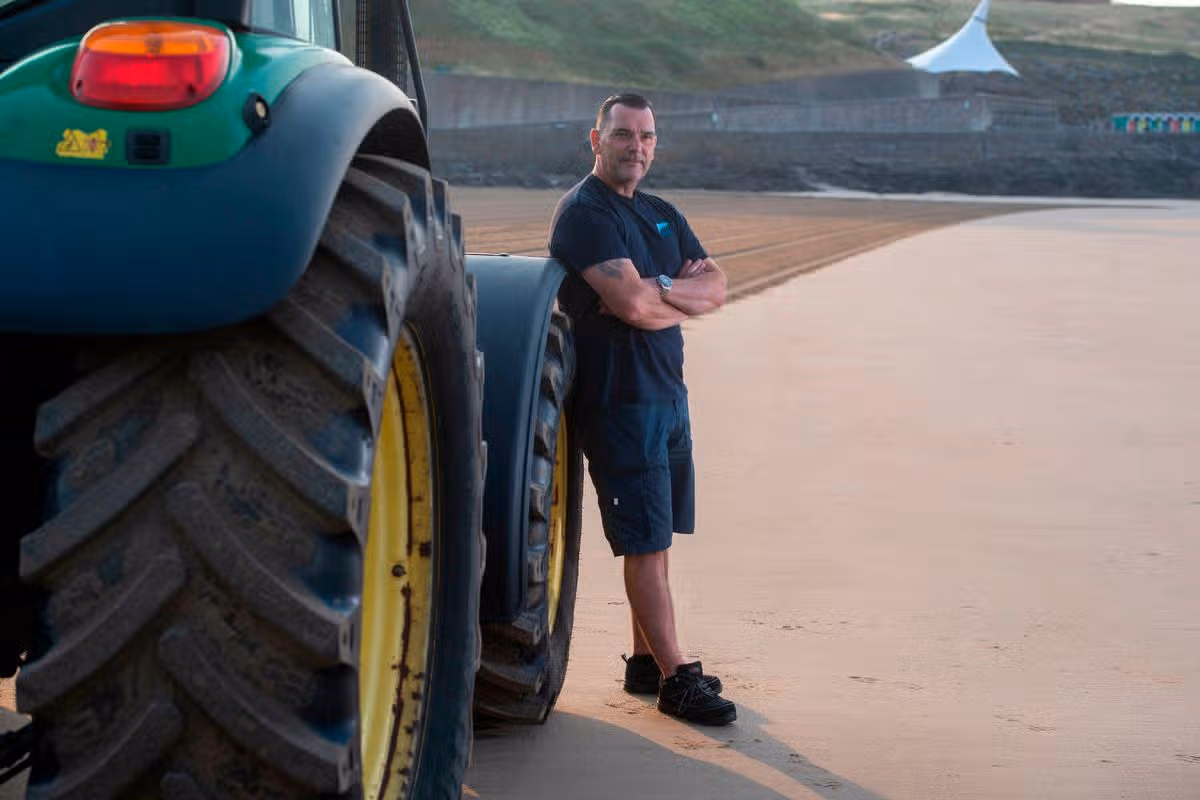 A man leaning against a tractor on a beach