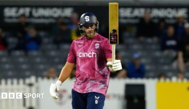 David Willey holding his bat aloft in his left hand after scoring a half-century for Northamptonshire Steelbacks