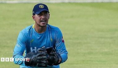 Kai Smith in action for Warwickshire in a T20 Blast game. He is wearing a light blue Bears top, navy trousers and wicket-keeper gloves and pads.