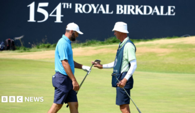 Two men on a golf course in front of a sign reading: '154th Royal Birkdale'.