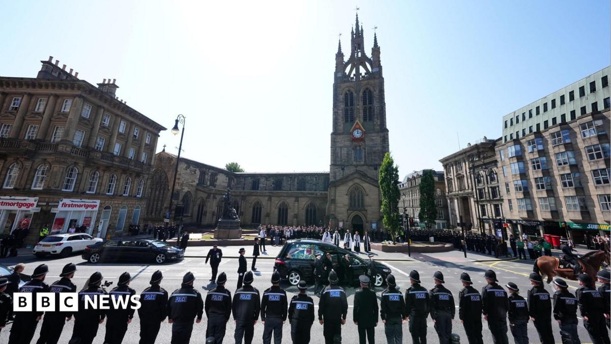 A funeral cortege arrives at Newcastle Cathedral as rows of police officers stand in formation, with mourners gathered outside the church during a ceremonial service. It is a sunny day. Attendees stand on the edge of the square in front of the cathedral, with clergy waiting for the cortege in the centre of the plaza.