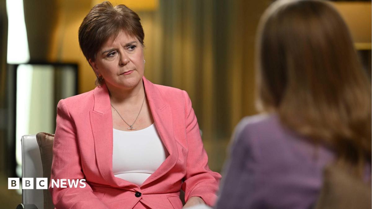 Nicola Sturgeon wearing a pink suit and white vest, with a quizzical expression. She is sitting on a chair facing another woman who has blonde hair and is wearing purple.