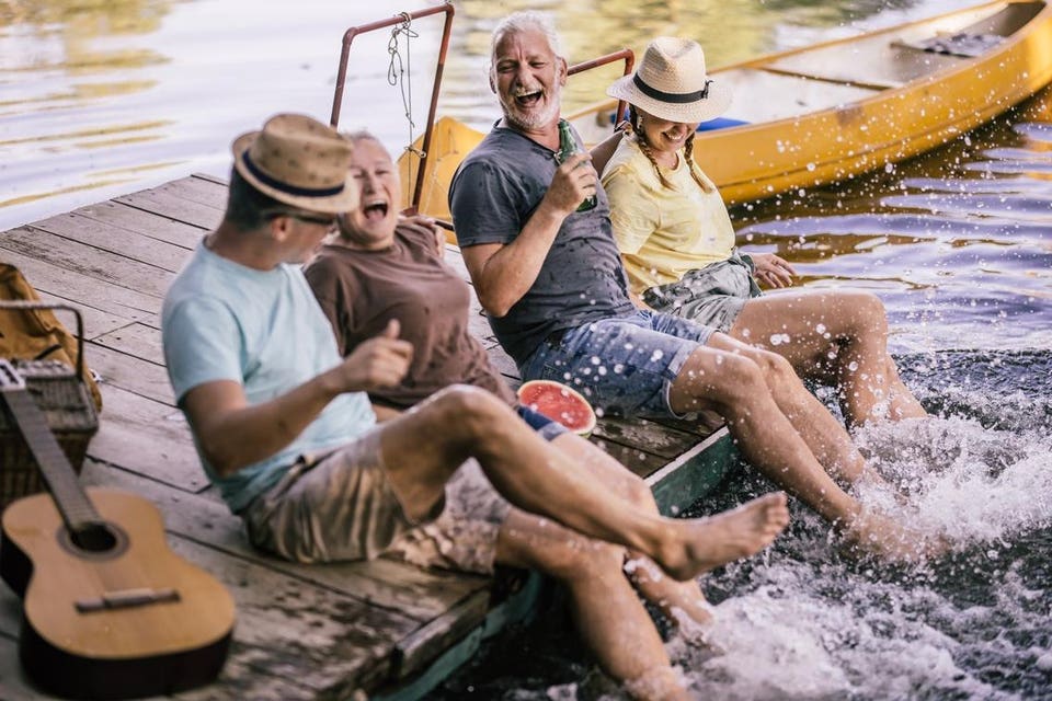 elderly friends sharing joy and music on a lakeside dock at sunset