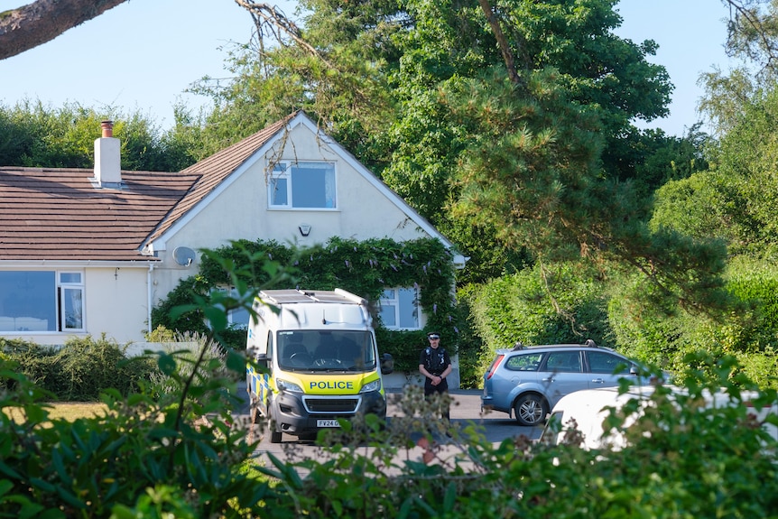 A police officer and police van sit outside a country cottage.