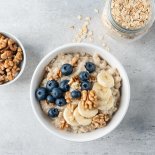 Oatmeal porridge with banana blueberry and walnuts in ceramic bowl. Top view. Grey concrete table background. Healthy eating, dieting concept