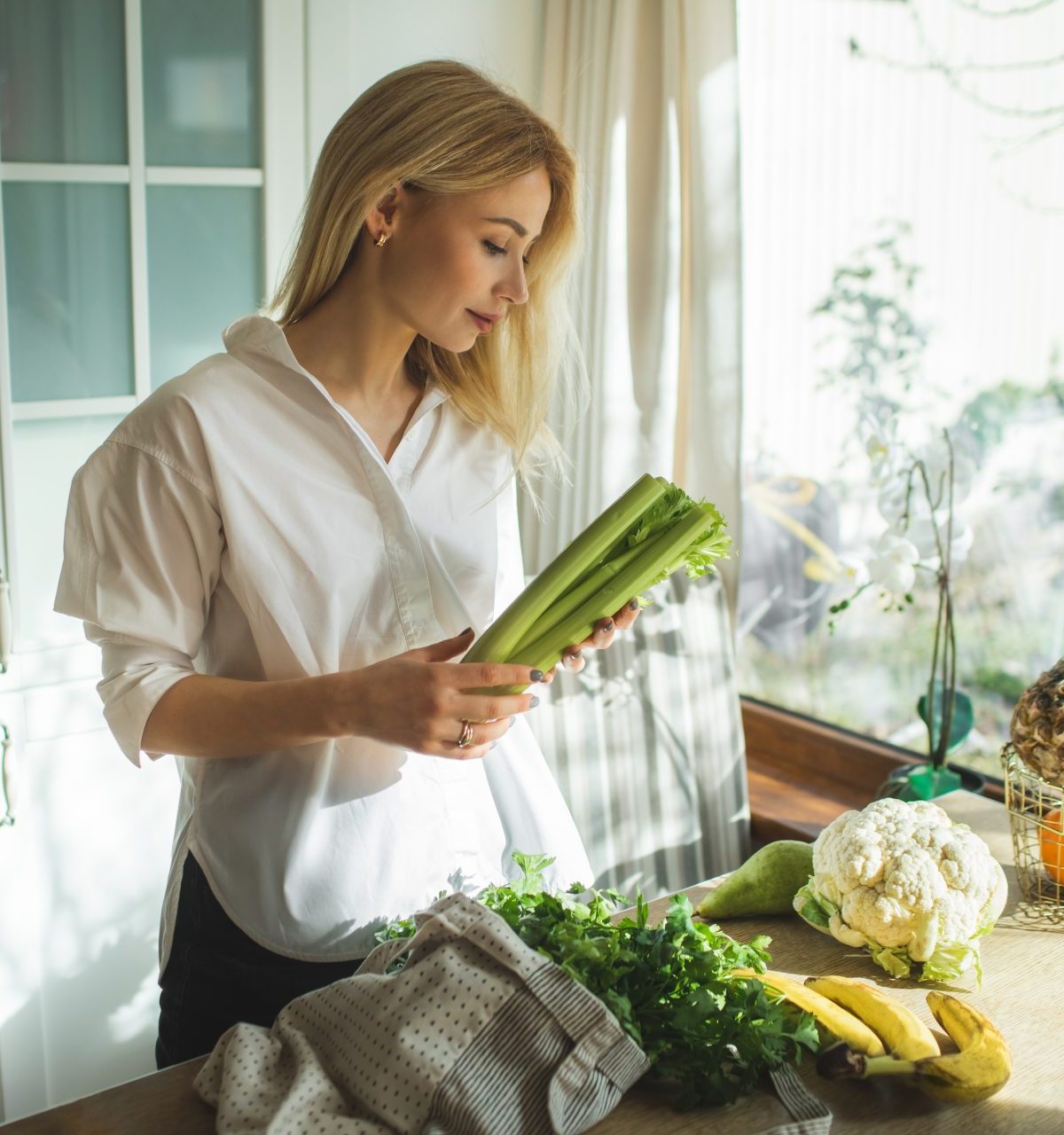 Beautiful woman unpacks a full fabric bag with fruits and vegetables on the kitchen. - stock photo