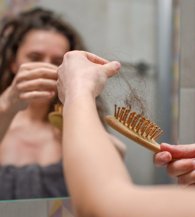 Young Upset Woman In Bathroom Holding Brush With Hair , Hair Loss And Hair Care Concept