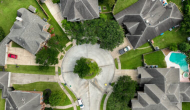 Aerial view of a residential cul-de-sac with houses, green lawns, trees, and a swimming pool