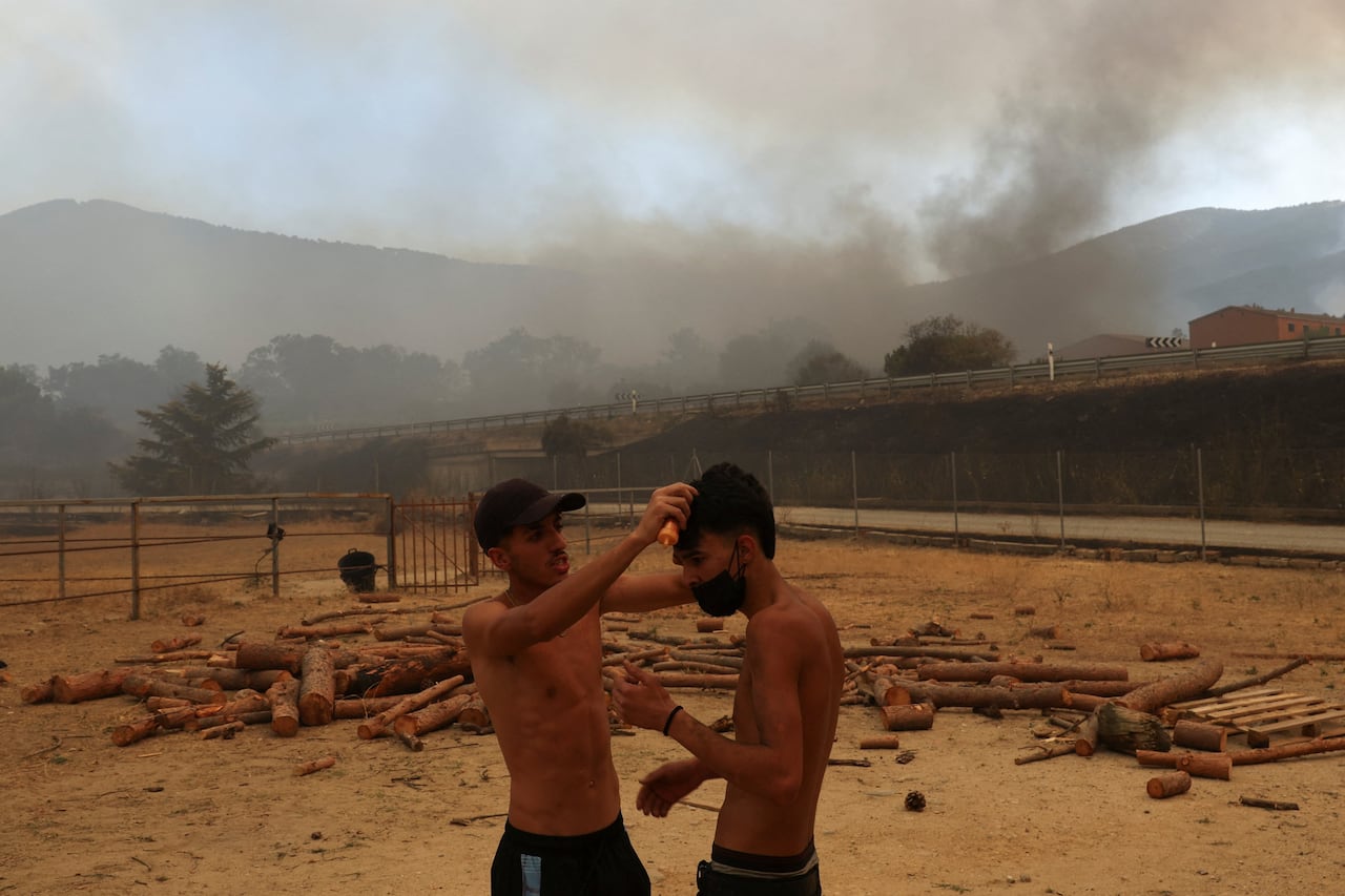Two shirtless men check each other for injuries. Behind them is wildfire smoke.