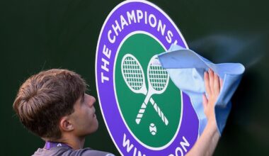 A person cleaning the Wimbledon Championships logo, featuring crossed tennis rackets and a ball.