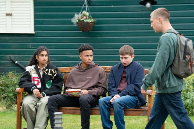 Avani, Denzel and Barney sat on a bench near Joel in EastEnders