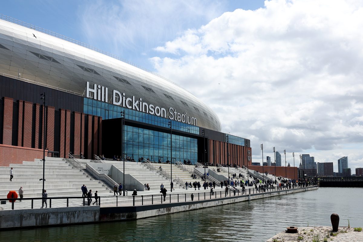 Hill Dickinson Stadium exterior, Liverpool, with fans on steps, waterfront, and city skyline.
