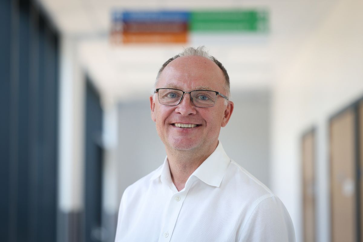 Middle-aged man with grey thinning hair and glasses in white smart shirt, smiling at camera